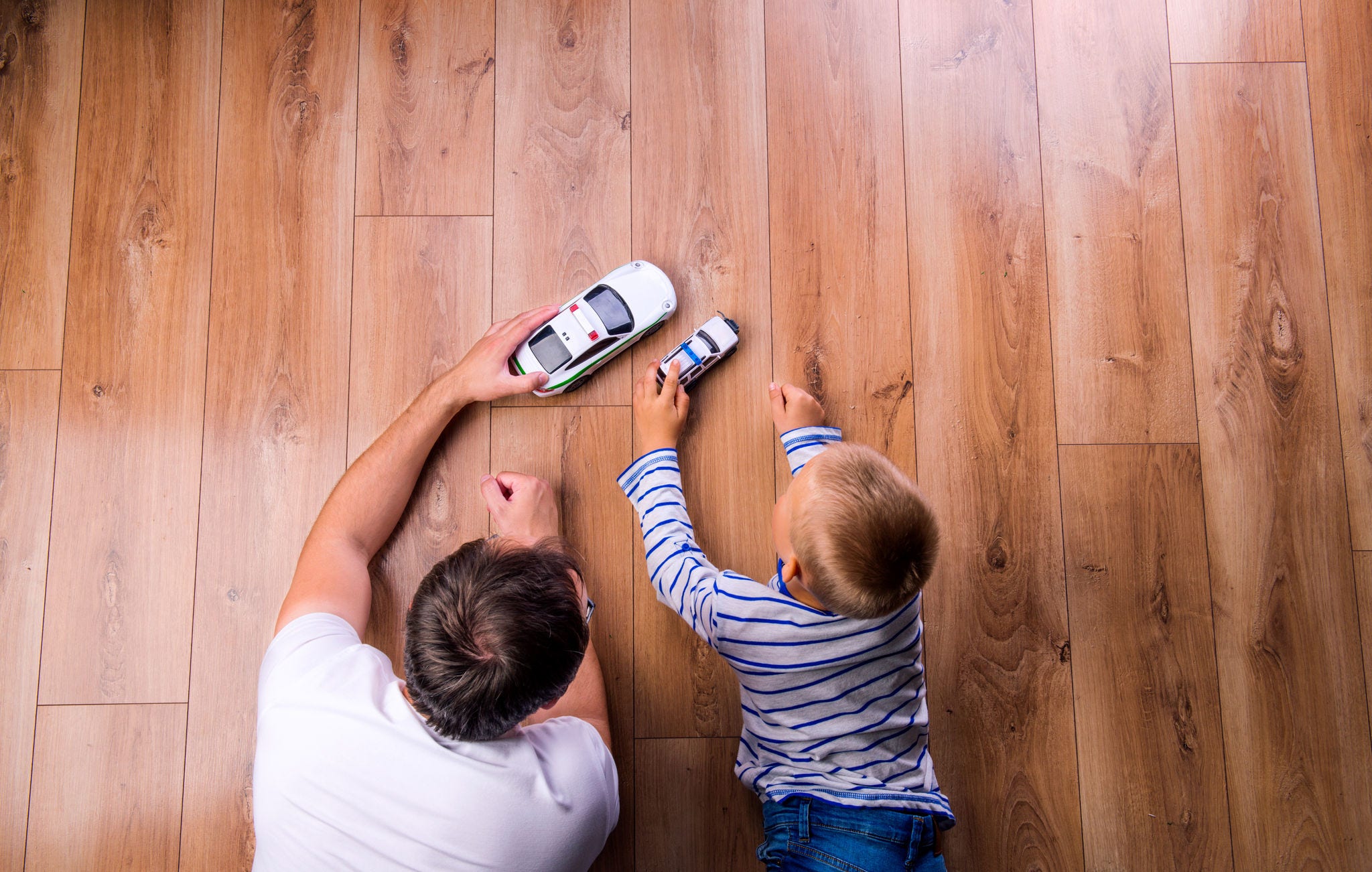 padre con su hijo jugando con autos en el piso de madera