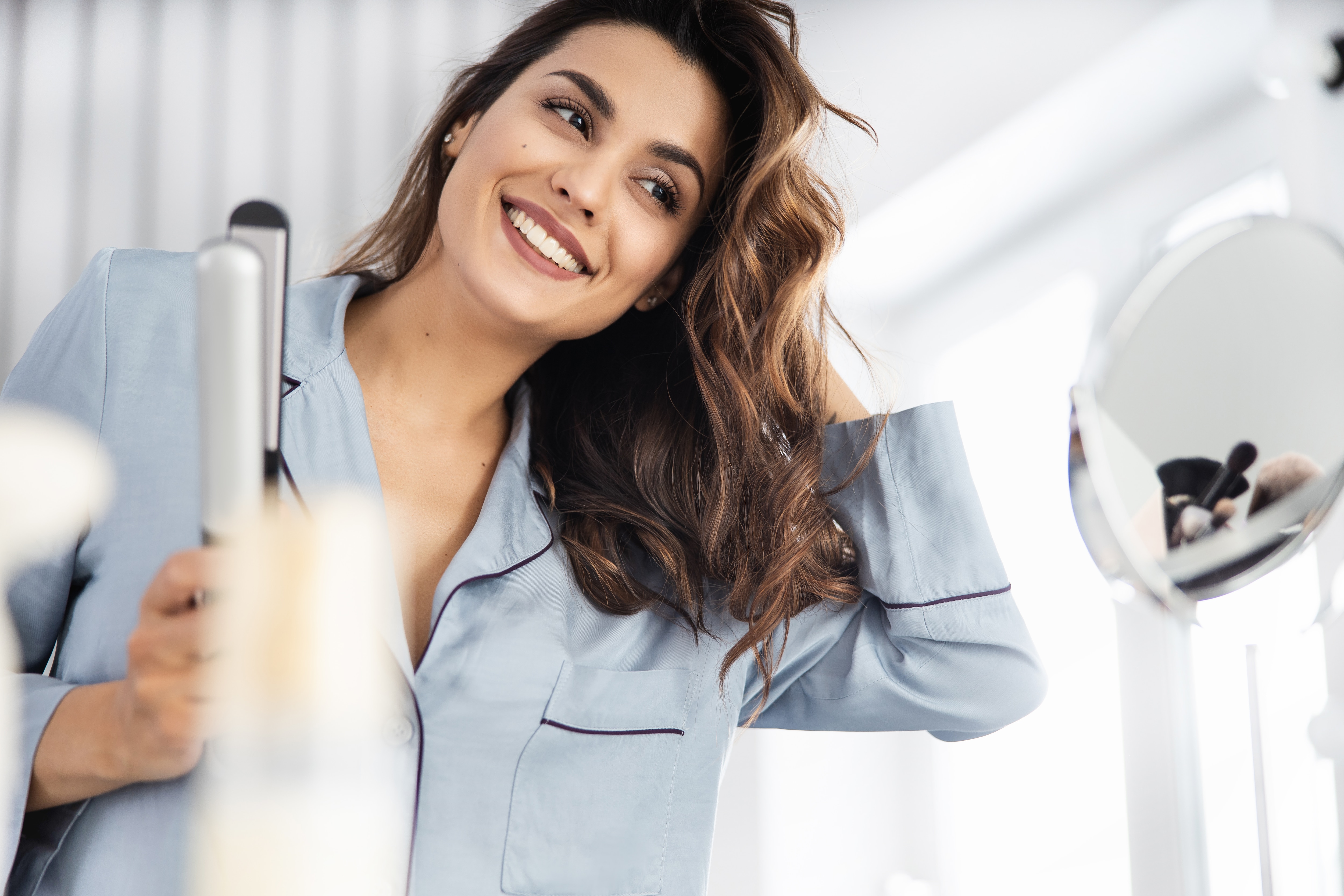 Happy pretty woman holding curling iron at home